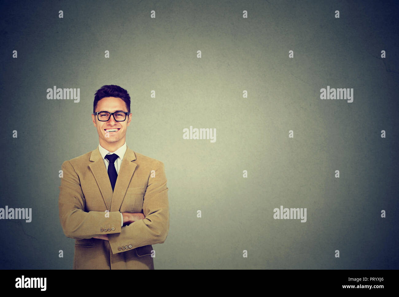 Fashionable young man in beige velvet jacket and glasses smiling at camera on gray background Stock Photo