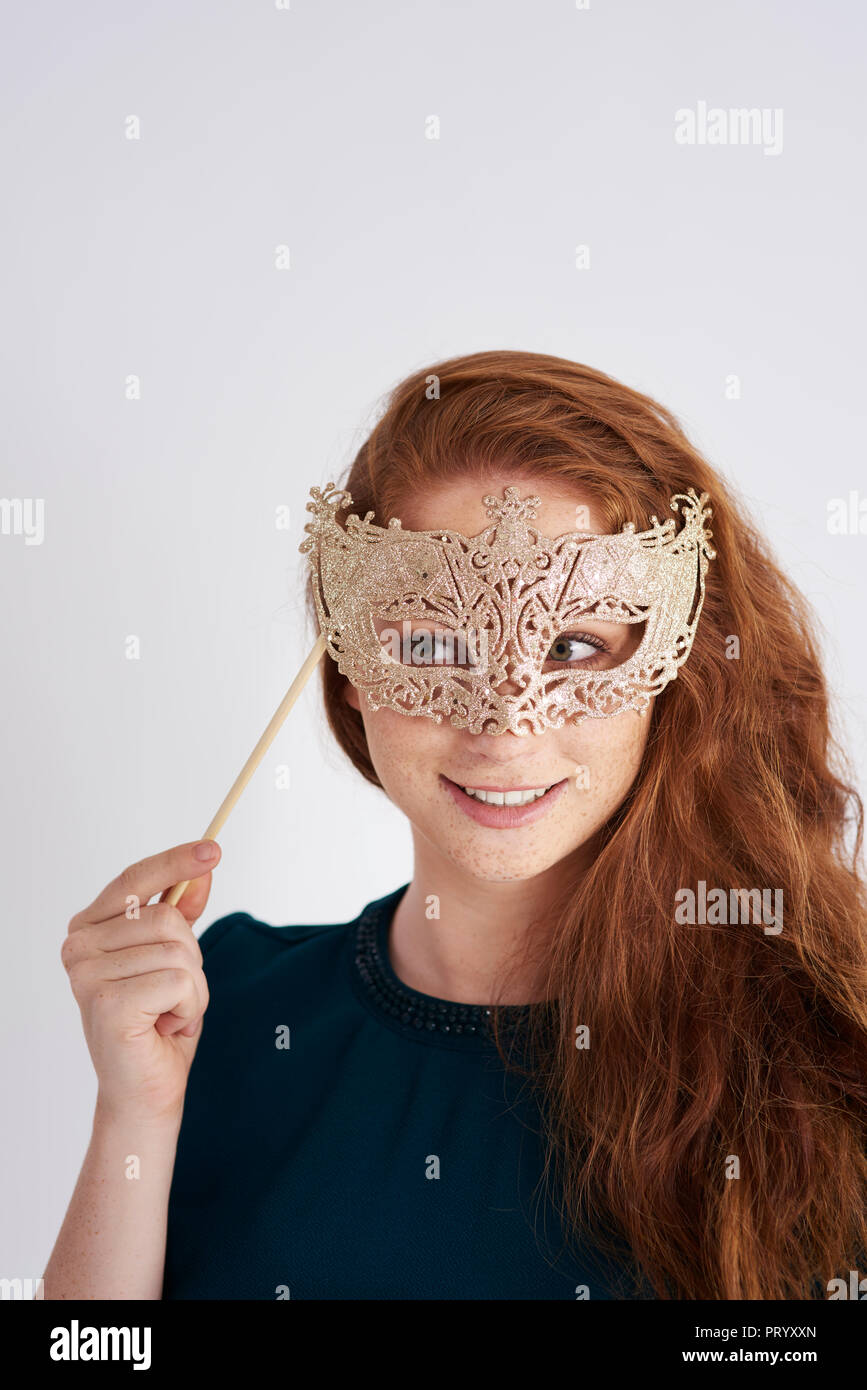 Portrait of smiling redheaded woman with masquerade mask Stock Photo