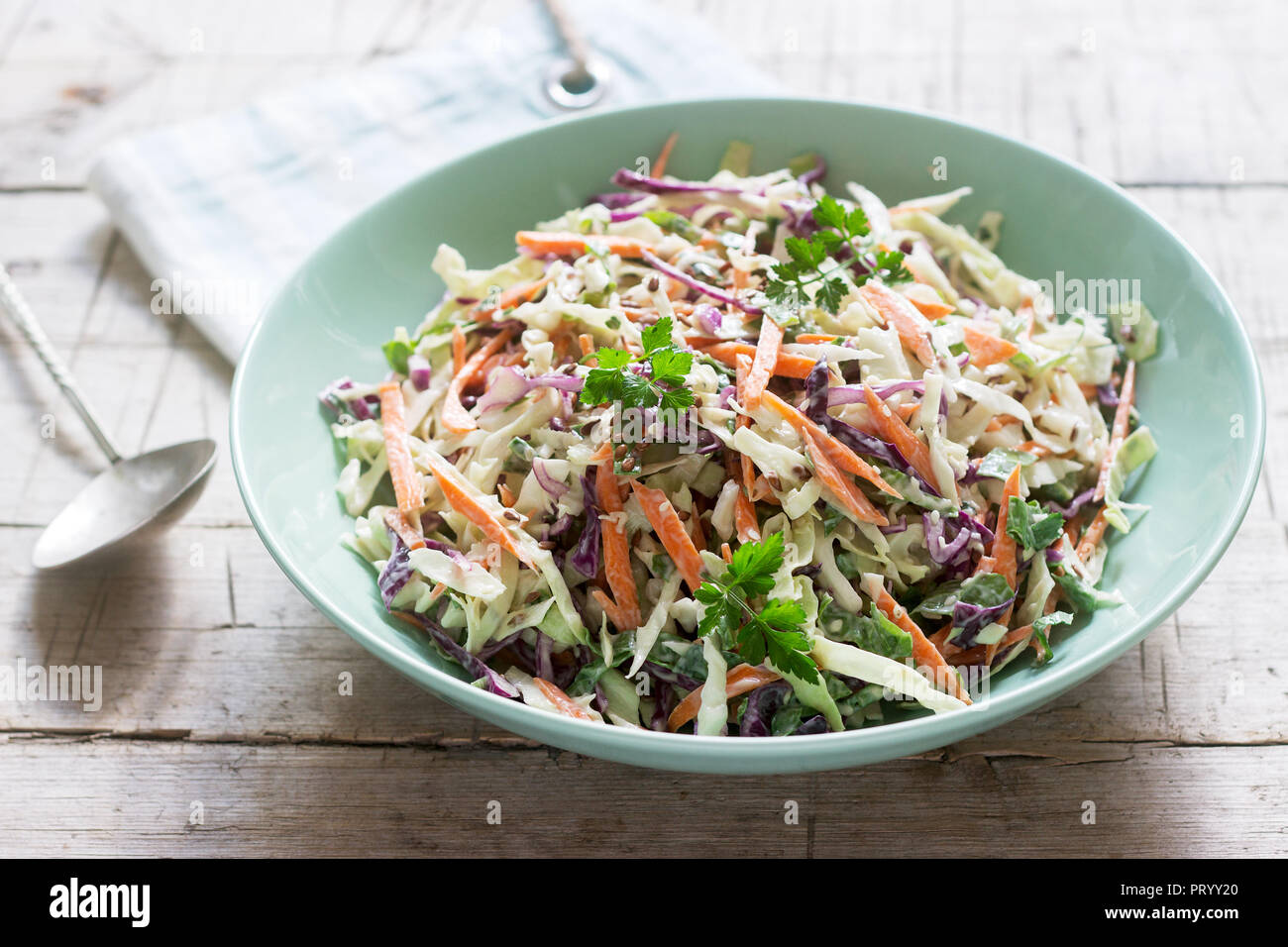 Coleslaw of cabbage, carrots and various herbs with mayonnaise in a large plate on a wooden background. Stock Photo