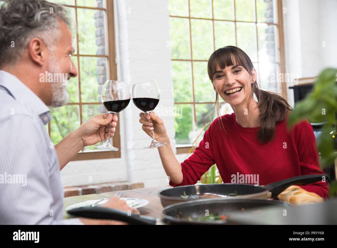 Happy couple sitting in kitchen, toasting with red wine, enjoying dinner Stock Photo