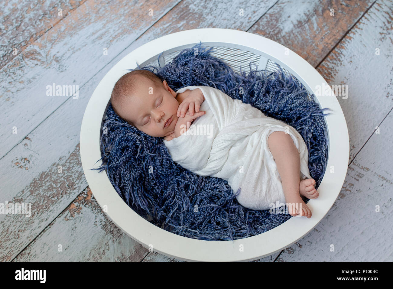 Little baby boy sleeping in a basket on the wooden floor, studio shot