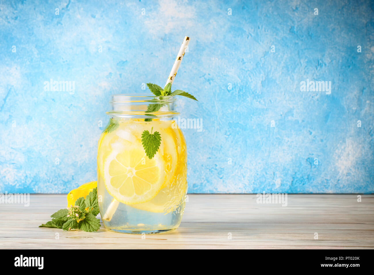 Coctail jar of lemonade and mint leaves on wooden table blue background Natural lemon water homemade food is popular detox beverage Glass of antioxidant infusion. Stock Photo