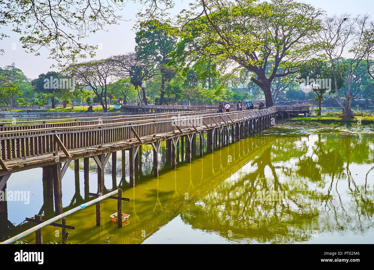 YANGON, MYANMAR - FEBRUARY 27, 2018: The Kandawgyi park boasts the system of old wooden bridges, connecting its indented banks and creating perfect wa Stock Photo