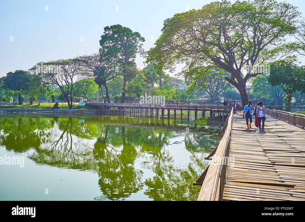 YANGON, MYANMAR - FEBRUARY 27, 2018: The wobbly creaking timber bridge across the lake is the local attraction of Kandawgyi park, on February 27 in Ya Stock Photo
