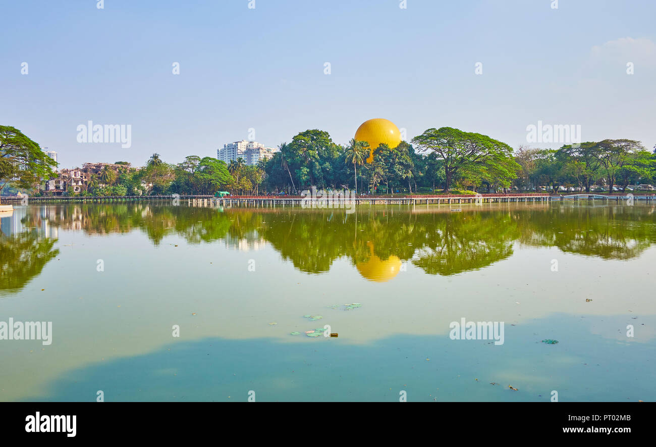 The clear surface of Kandawgyi Lake reflects the blue sky and lush greenery of park on the lake's banks, Yangon, Myanmar Stock Photo