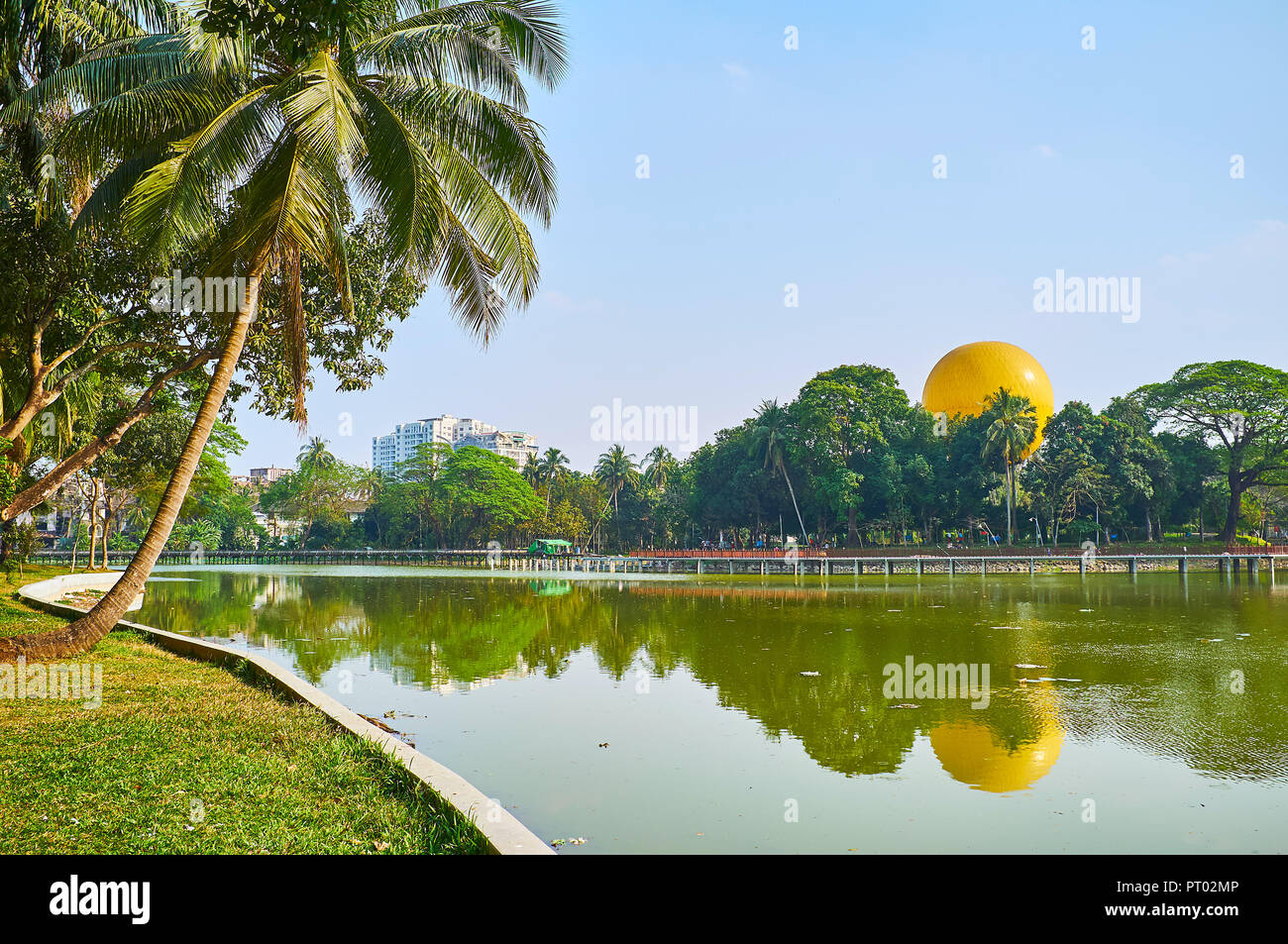 Lush tropic garden with palm trees and other local species covers the banks of Kandawgyi Lake, one of the major lakes in Yangon, Myanmar. Stock Photo