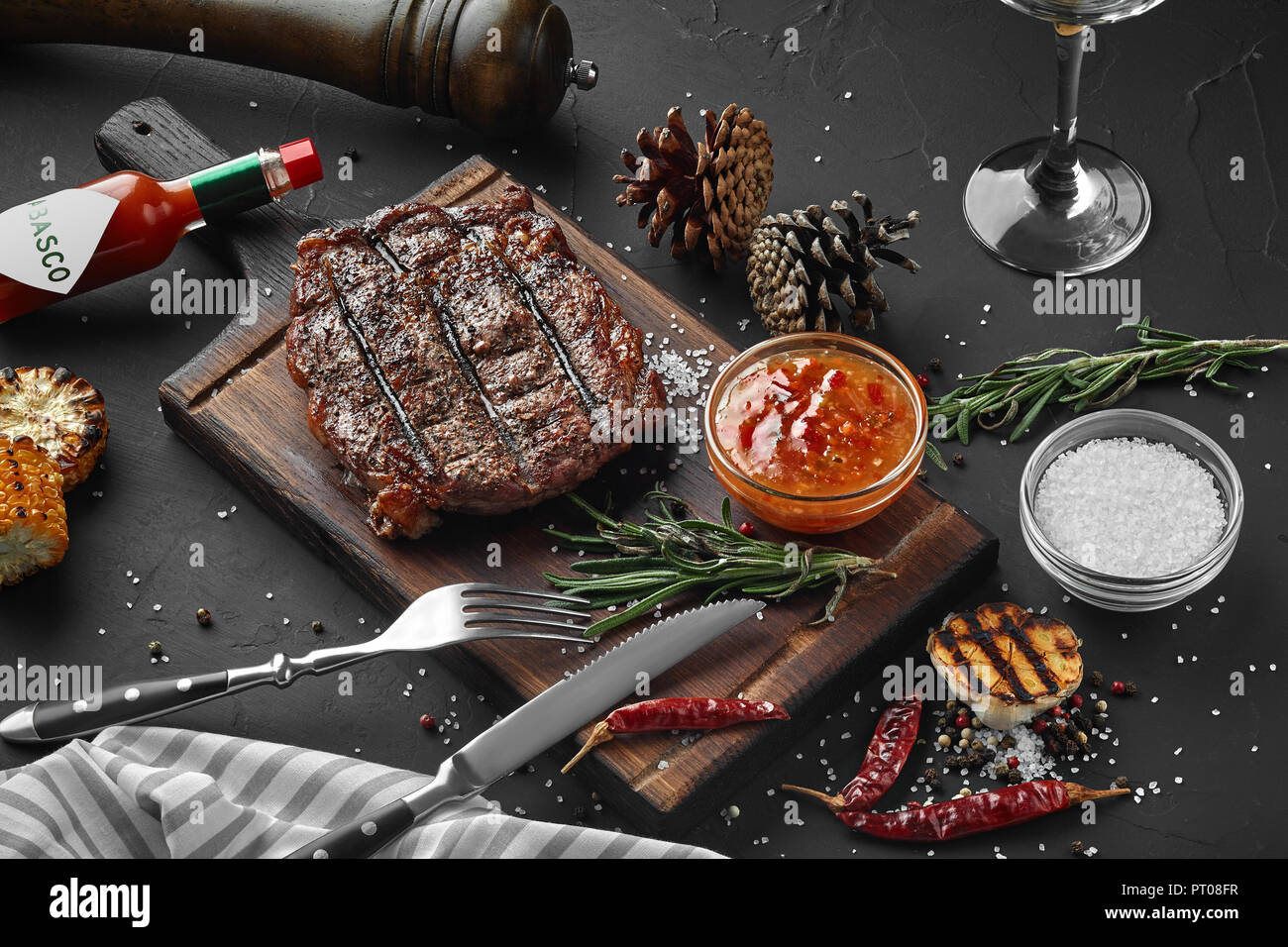 Medium rare grilled Steak Ribeye with corn and garlic on serving board block on black background. Top view. Still life. Flat lay Stock Photo