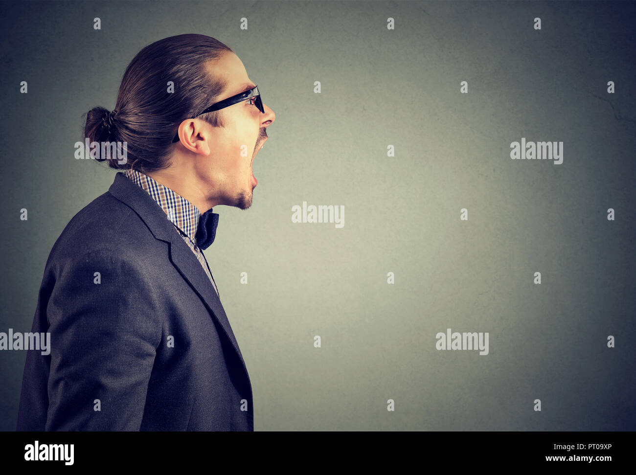 Side view of an angry man in rage shouting loudly with mouth opened on gray background. Stock Photo