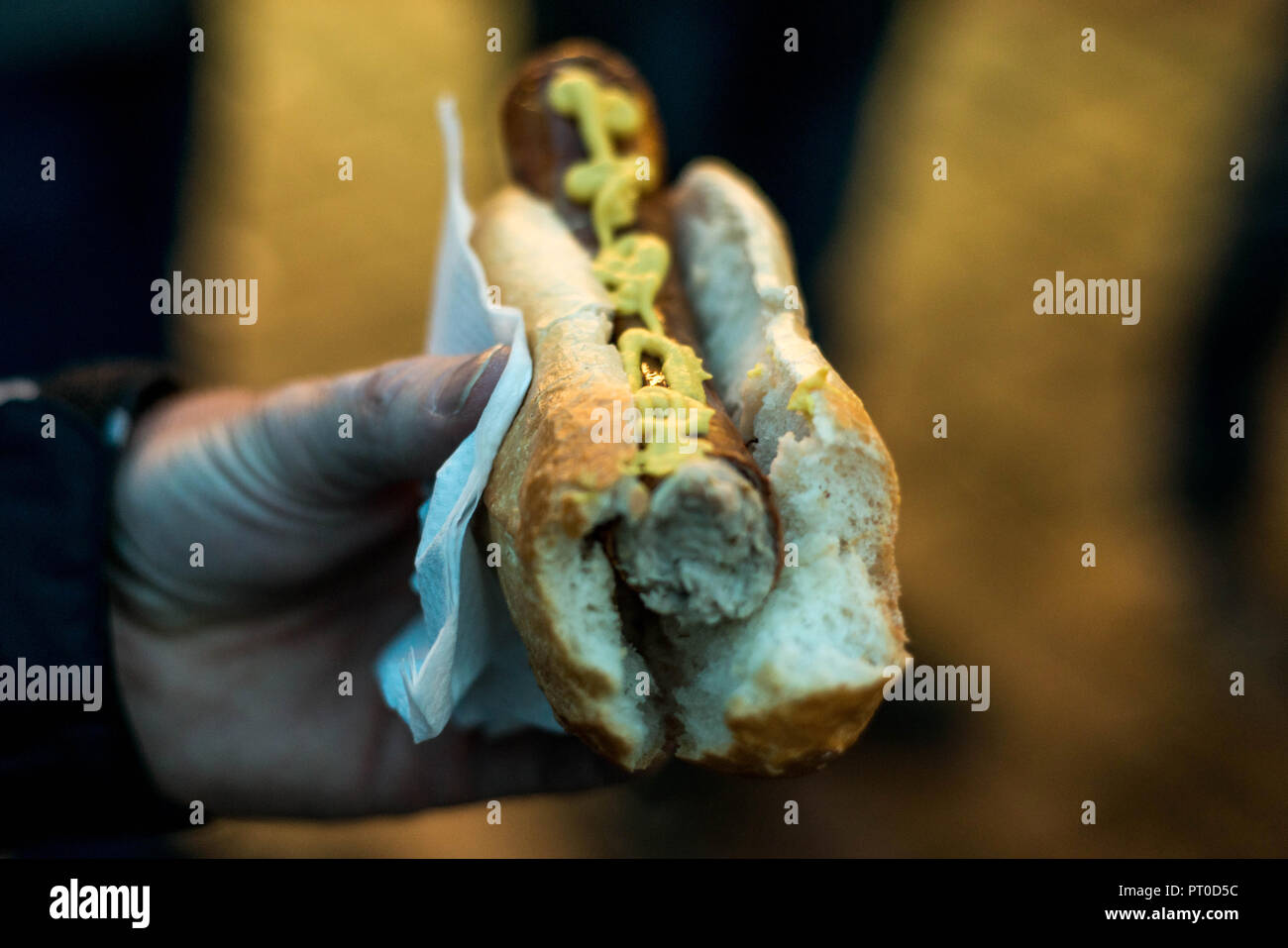 Person Hand Holding Bratwurst or Rostbratwurst a Traditional German Sausage, with Mustard on a Bun on a christmas market. Stock Photo