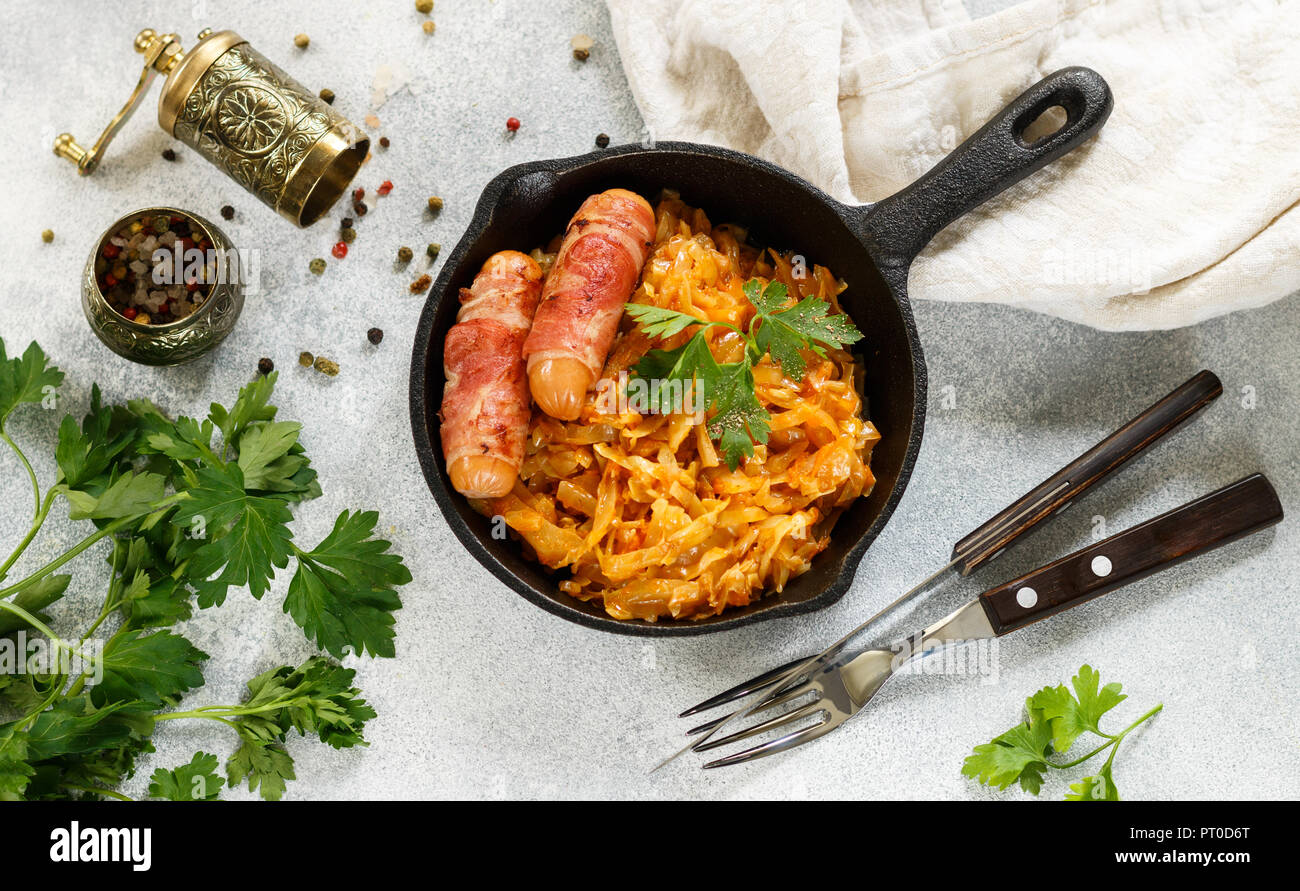 Stewed cabbage with carrots, onions and tomatoes and sausages in bacon
