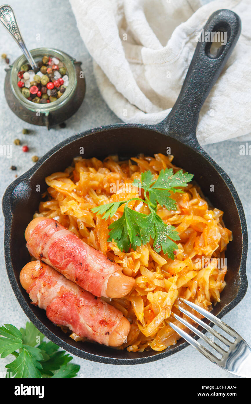Stewed cabbage with carrots, onions and tomatoes and sausages in bacon