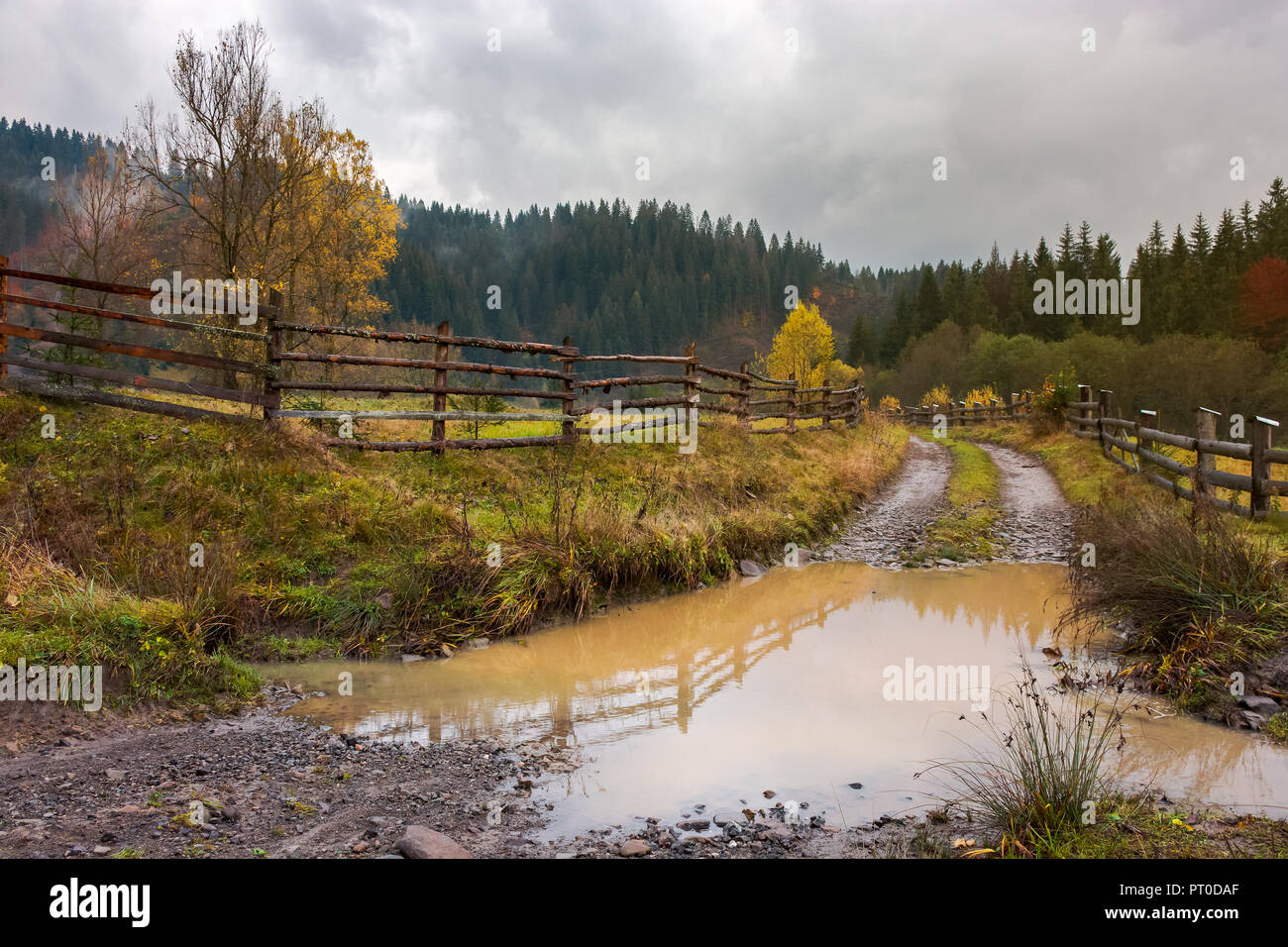 huge puddle on the country road. wooden fence along the path. deep autumn in mountainous countryside Stock Photo
