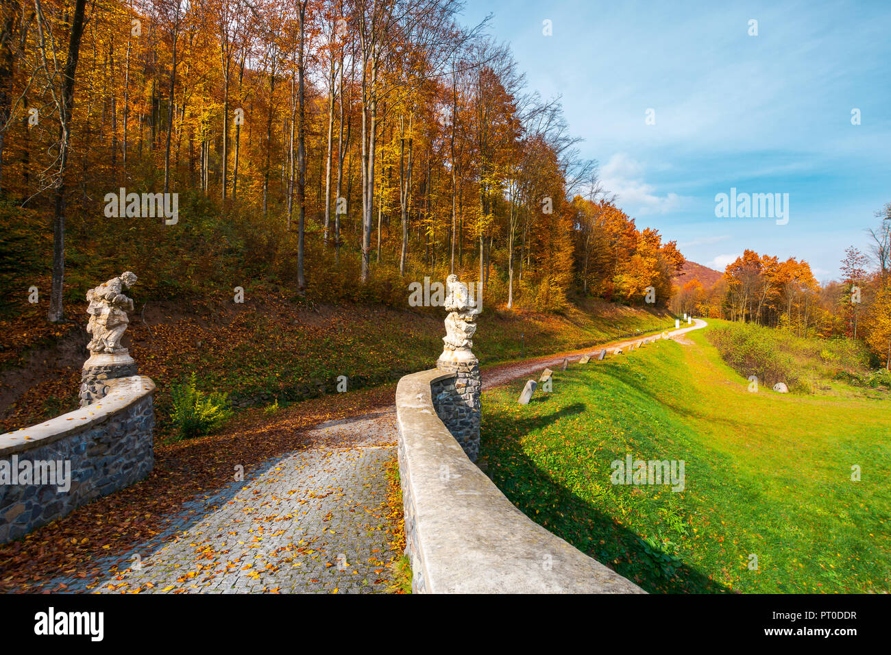 path from the stone bridge in to the forest. trees in fall colors. blue sky above the landscape Stock Photo