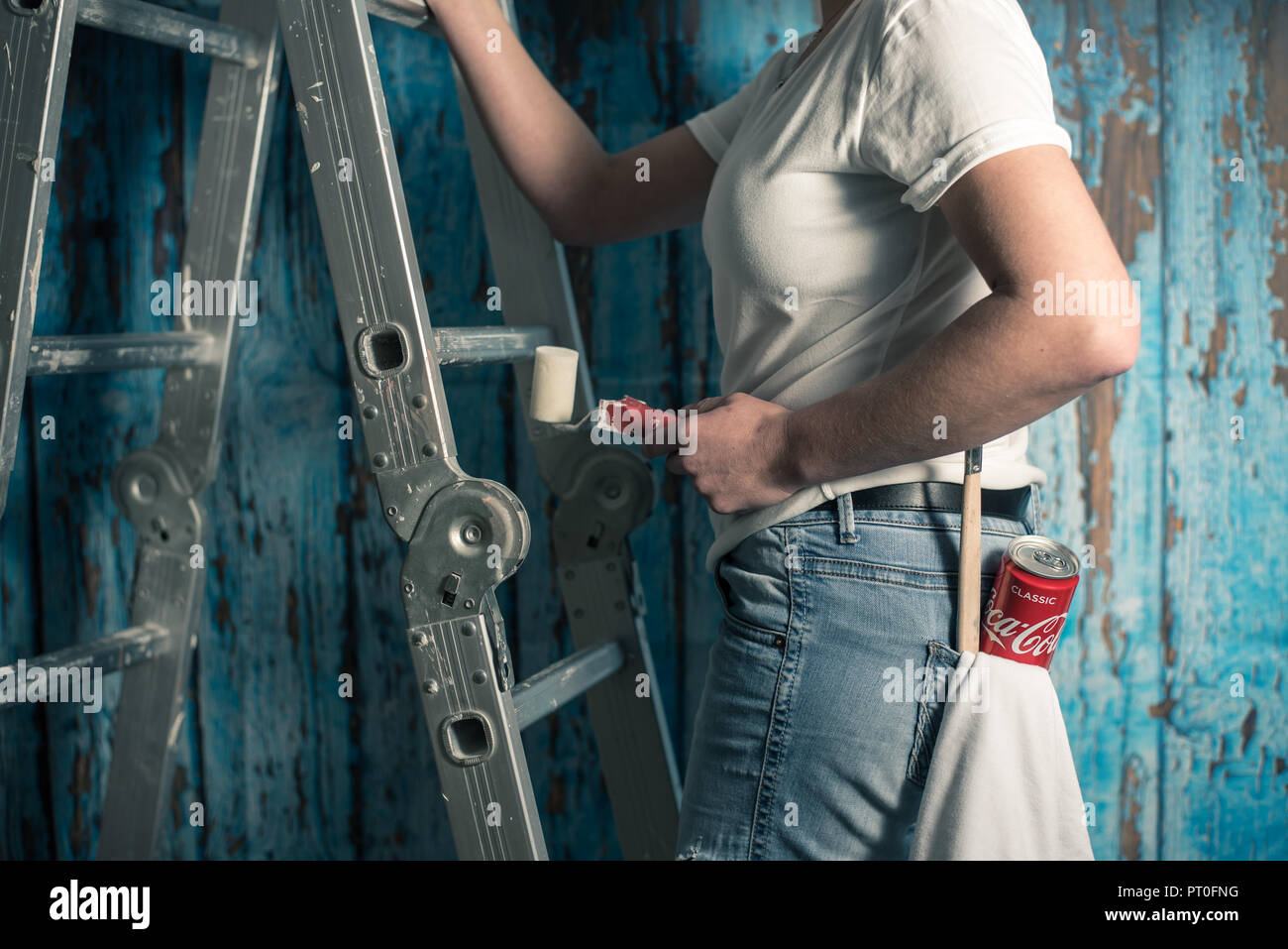 A woman painting a flat is standing next to a ladder with a paint roller and Coca Cola can Stock Photo