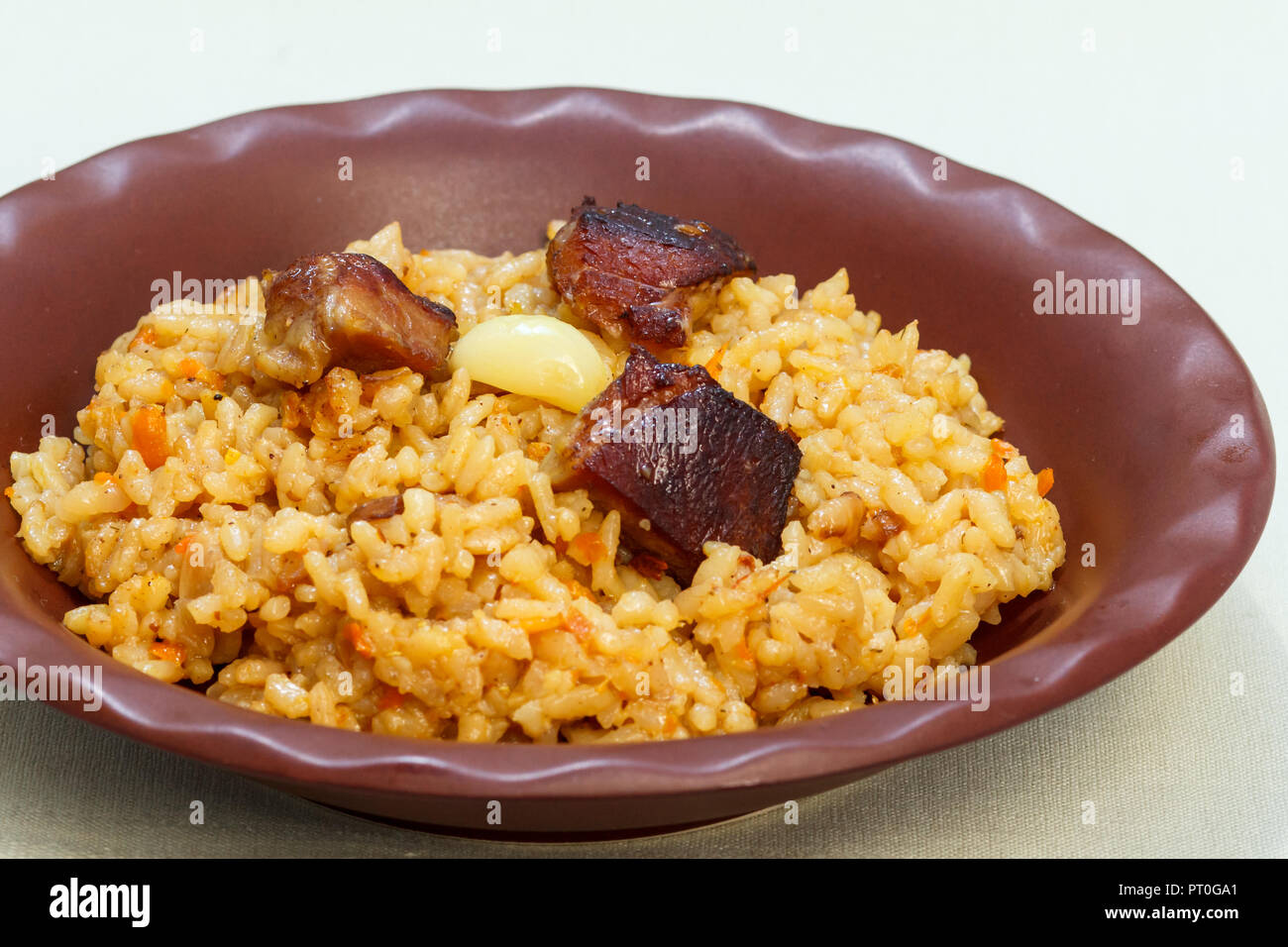 Rice pilaf with meat and vegetables on clay plate on white napkin Stock Photo