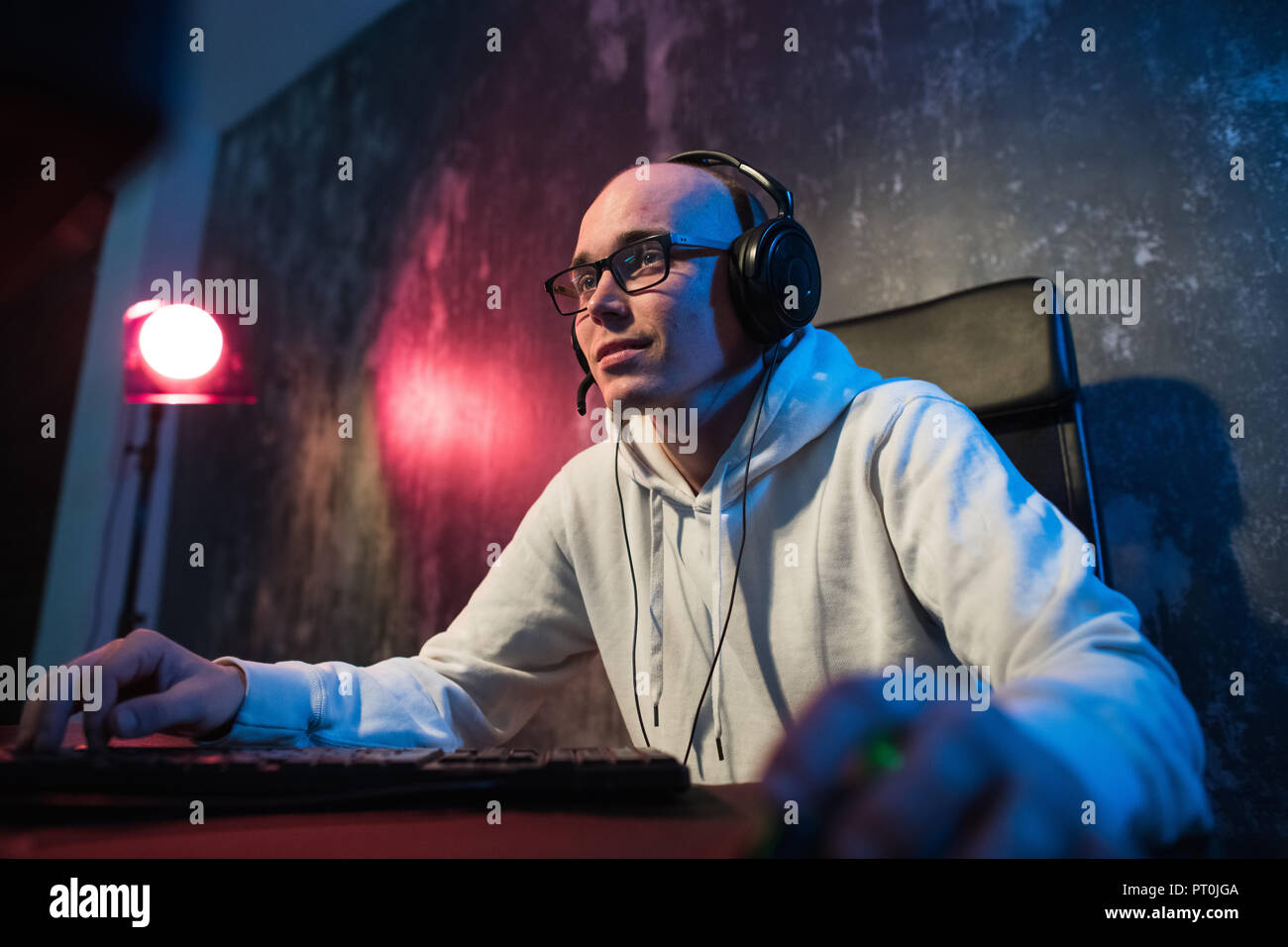 Professional Boy Gamer Plays in Video Game on a eSports Tournament or in Internet Cafe. He Wears Headphones and Speaks Commands into Microphone. Stock Photo