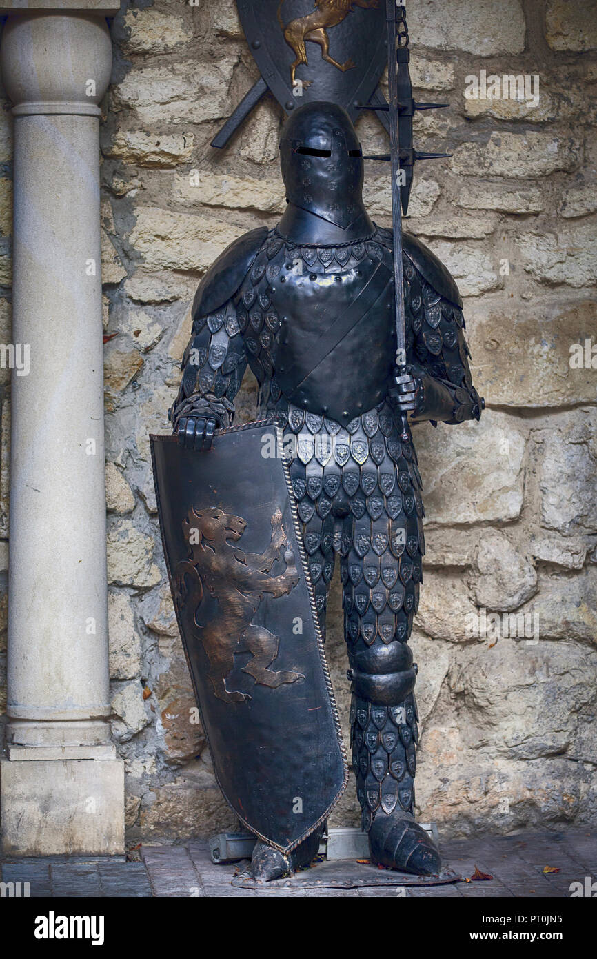 Ukraine, Lviv - October 4, 2018. Knight in full armor with a sword against the background of the ancient walls of a stone castle. Suit of knight armou Stock Photo