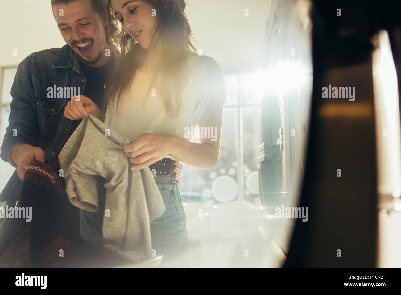 Smiling man and woman putting clothes in a washing machine together