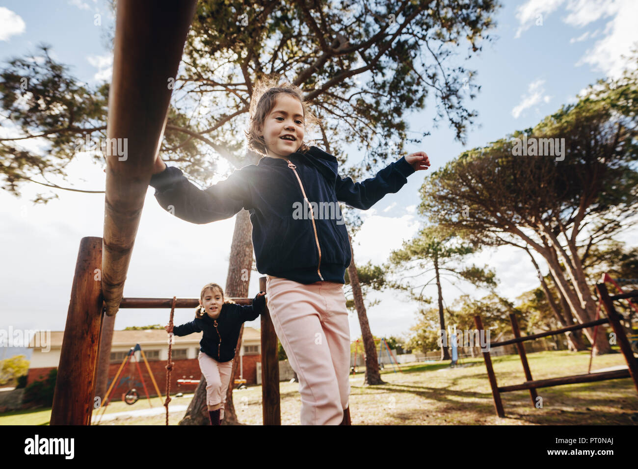 Cute little girl with her twin sister playing at playground outdoors on sunny day. Twin girls playing at the public park. Stock Photo
