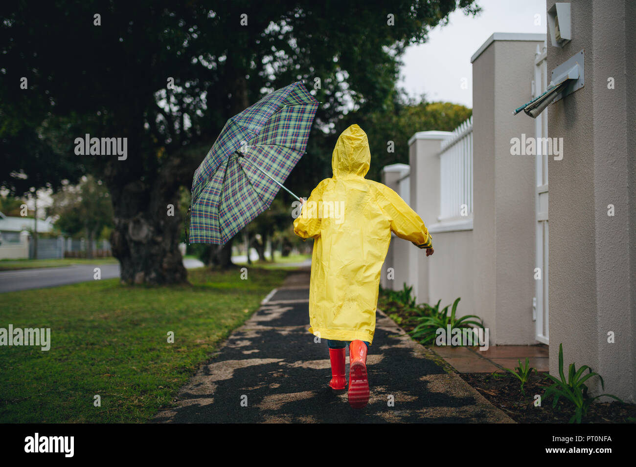 Rear view of little girl running outdoors on a rainy day. Girl wearing