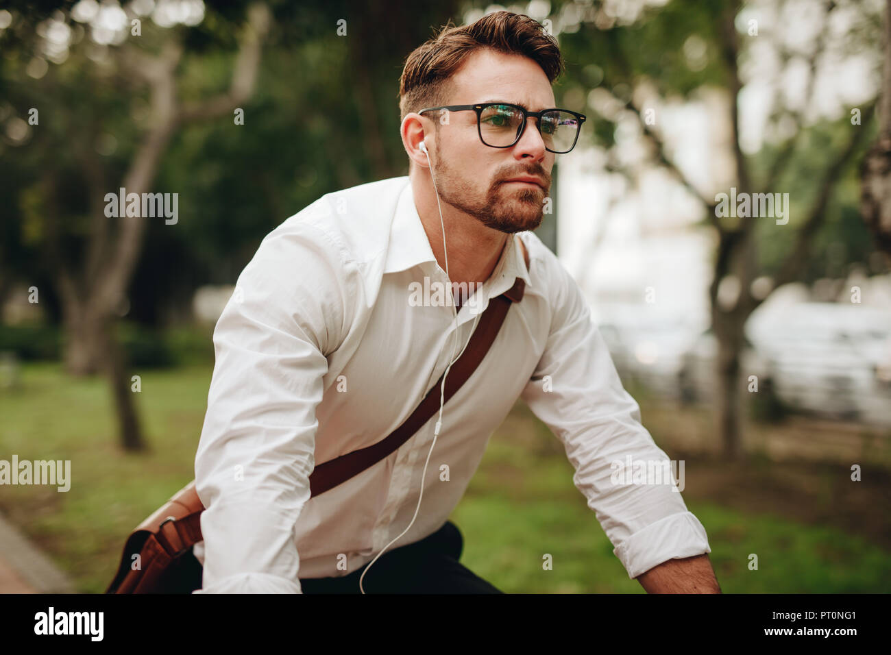 Businessman commuting to office on a bike listening to music. Man riding a two wheeler listening to music on earphones. Stock Photo