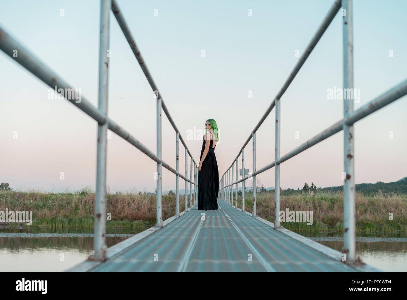 Young woman with dyed green hair standing on a footbridge looking back ...