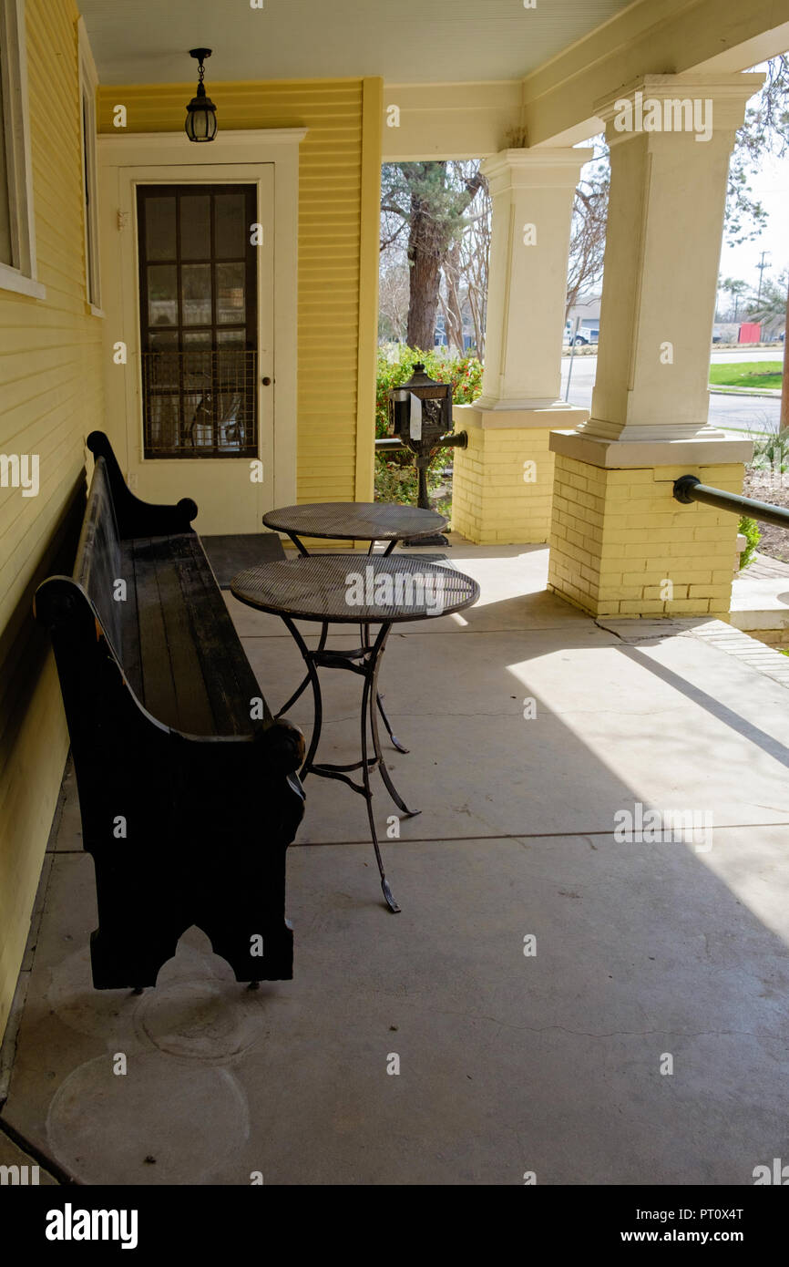 Historic house veranda, long wooden bench & 2 round tables. Yellow shingles & bricks. Dulaney House Chestnut Square Historic Village, McKinney Texas Stock Photo