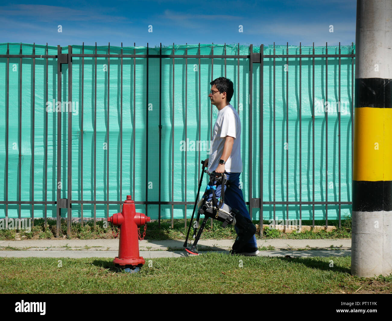 a man with crutches walking on a sidewalk on a morning with fire hydrant Stock Photo