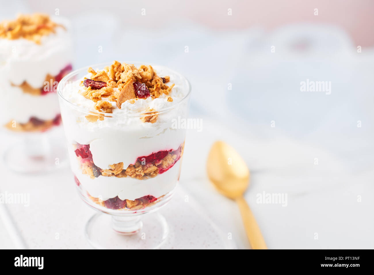 Close up of healthy raspberry yogurt parfait in a glass with golden spoon on white marble table over pink background with copy space. Stock Photo