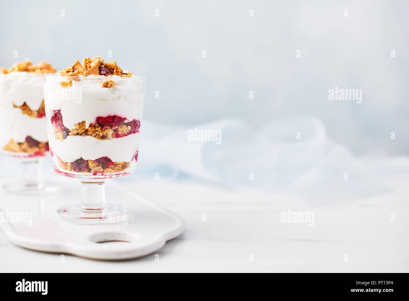Healthy raspberry yogurt parfait in a glass on white marble table over light blue background with copy space. Stock Photo