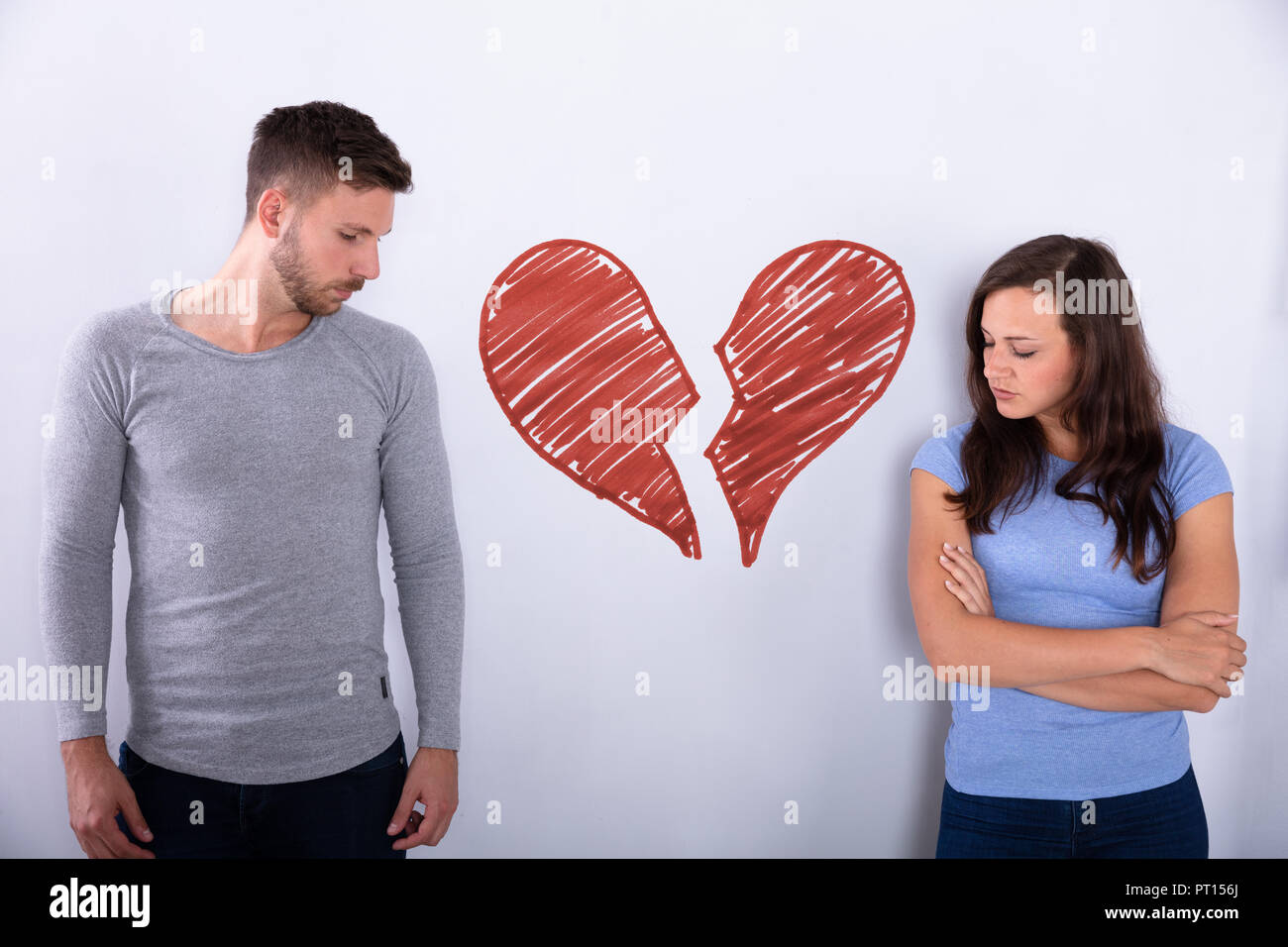Broken Red Heart Drawn On Wall Between Sad Young Couple Stock Photo