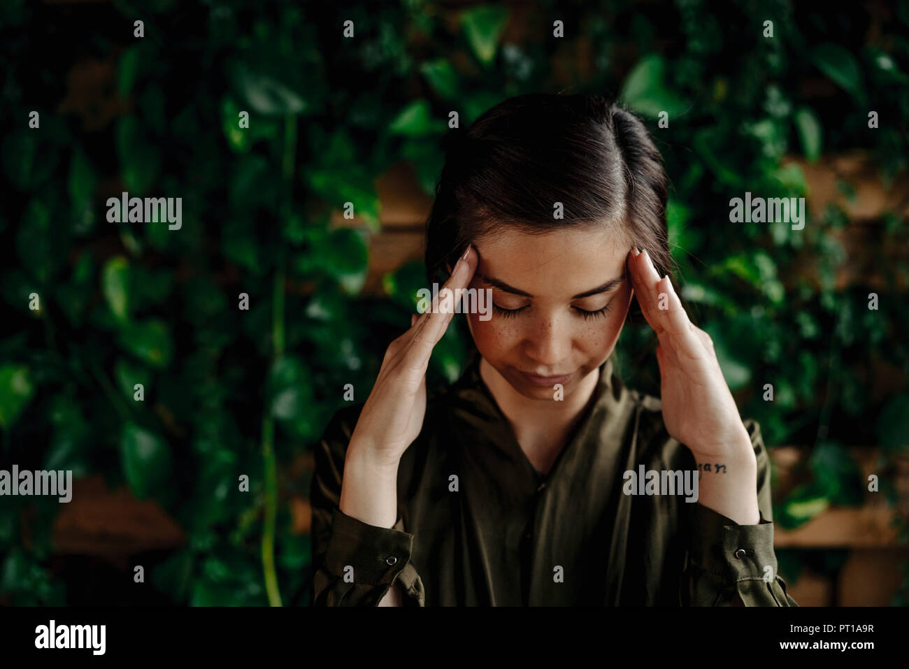 Focused young woman at wall with climbing plants Stock Photo
