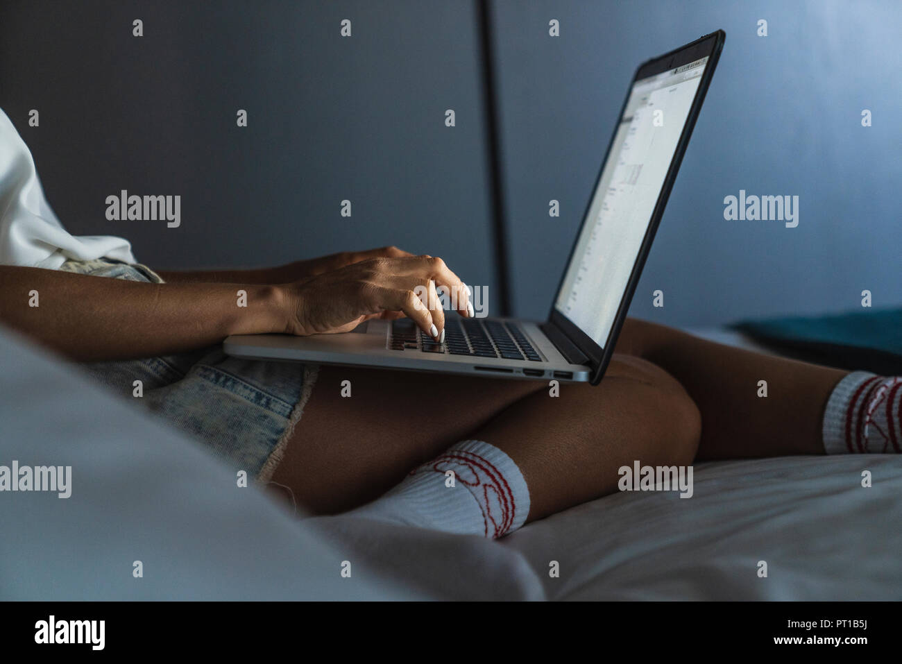 Woman sitting on bed, using laptop Stock Photo