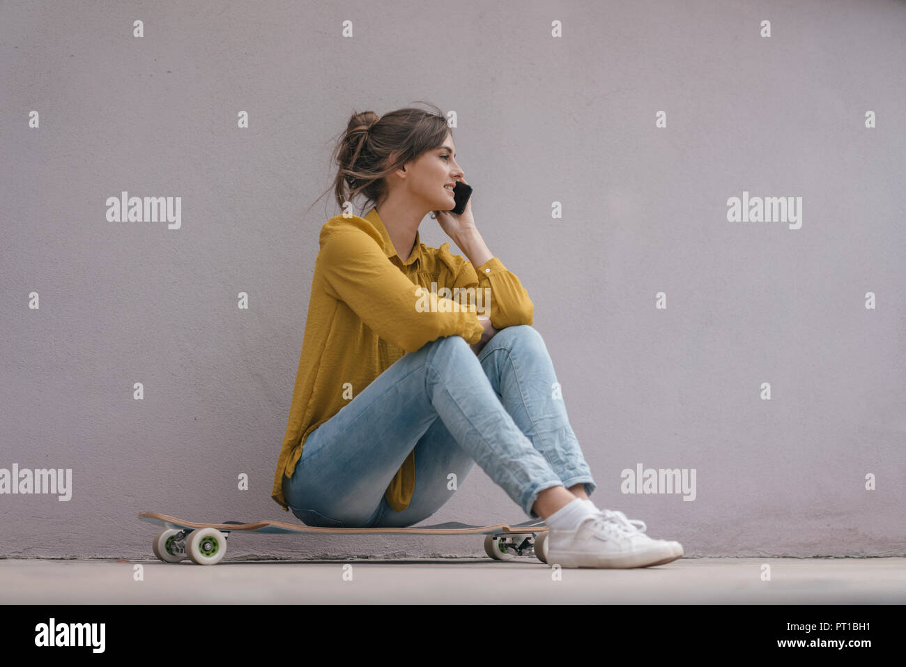 Young woman sitting on skateboard, using smartphone Stock Photo