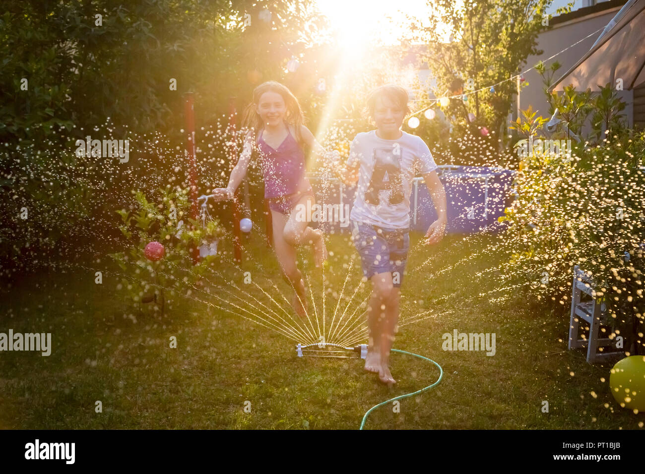 Brother and sister having fun with lawn sprinkler in the garden Stock ...