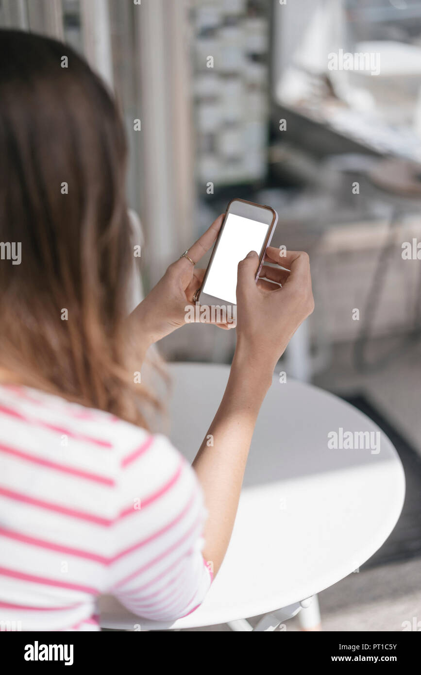 Young woman sitting in coffee shop, using smartphone Stock Photo