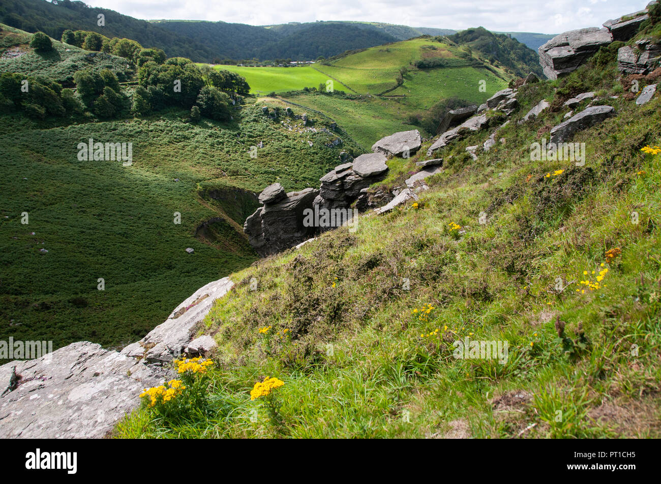 View down the steep slopes of a valley from high vantage point over rocky outcrops and fields and traditional stone walls. Stock Photo