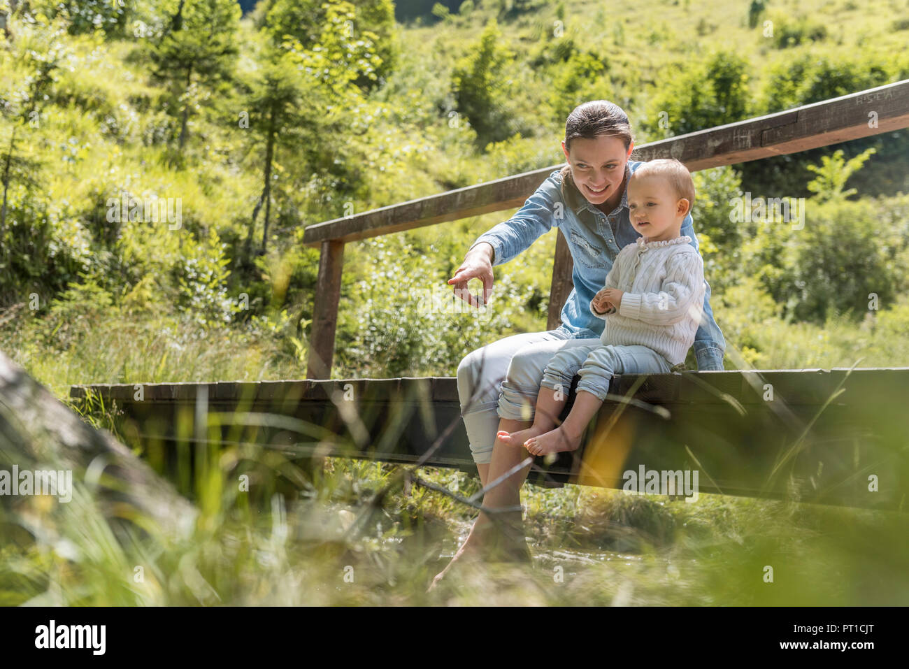 Mother and daughter sitting on wooden bridge Stock Photo