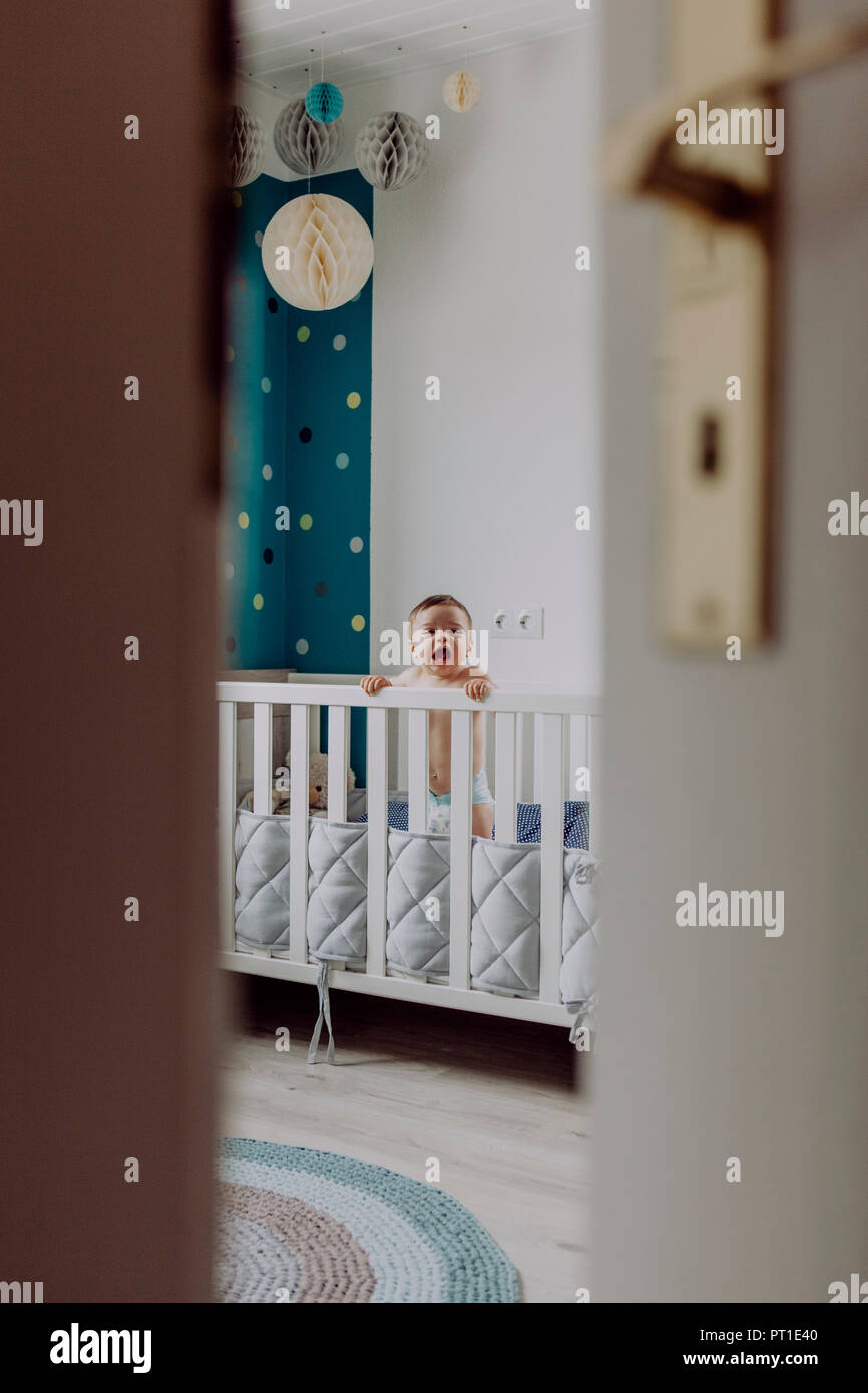 Baby boy standing in his cot, laughing Stock Photo