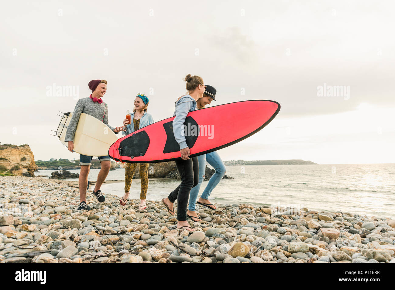 Happy friends with surfboards walking on stony beach Stock Photo
