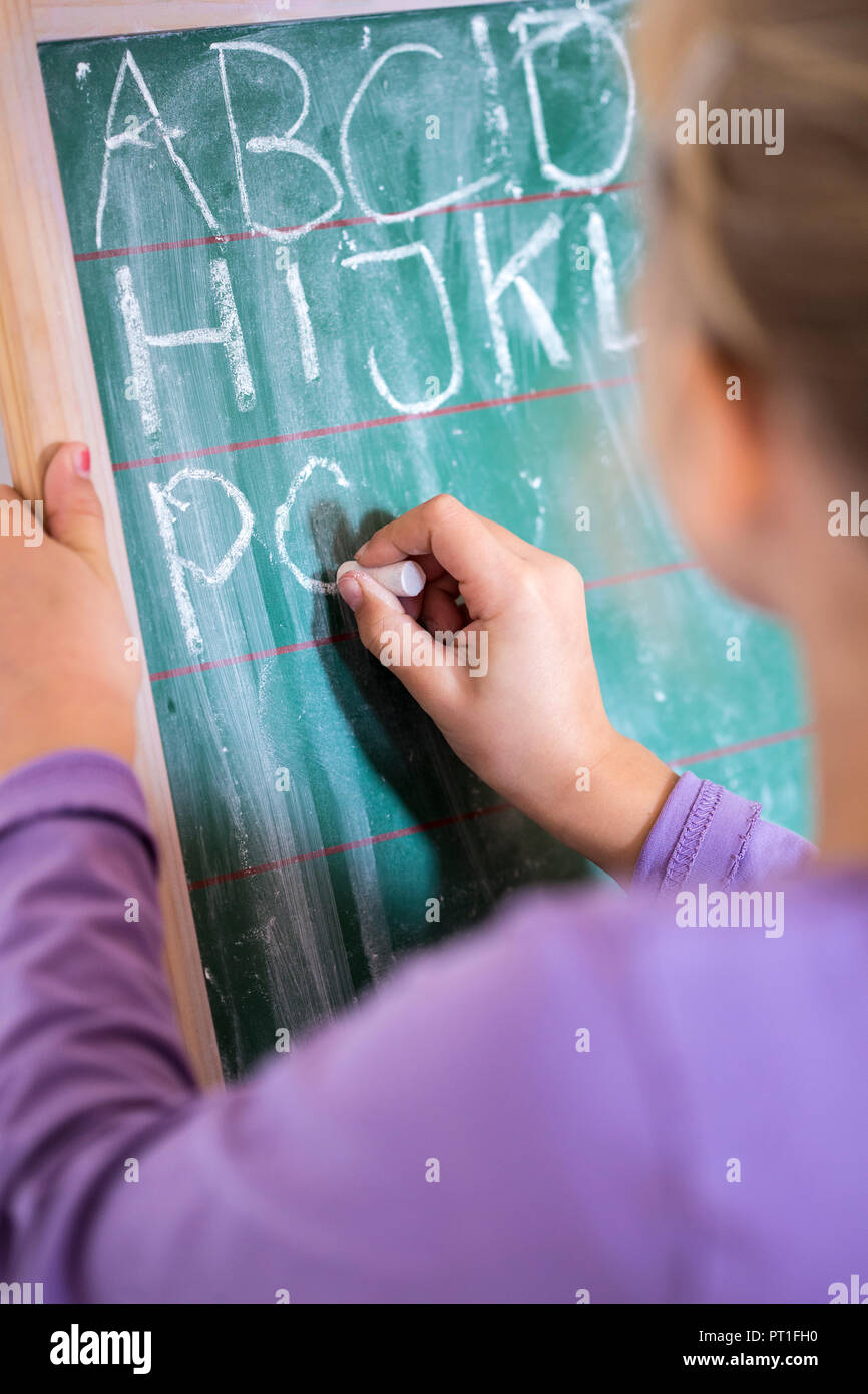 Back view of girl writing alphabet on chalkboard Stock Photo