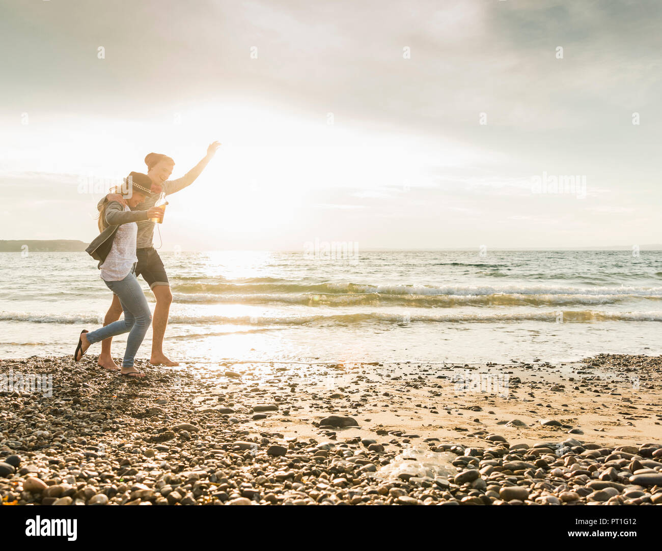 Happy young couple walking on the beach at sunset Stock Photo