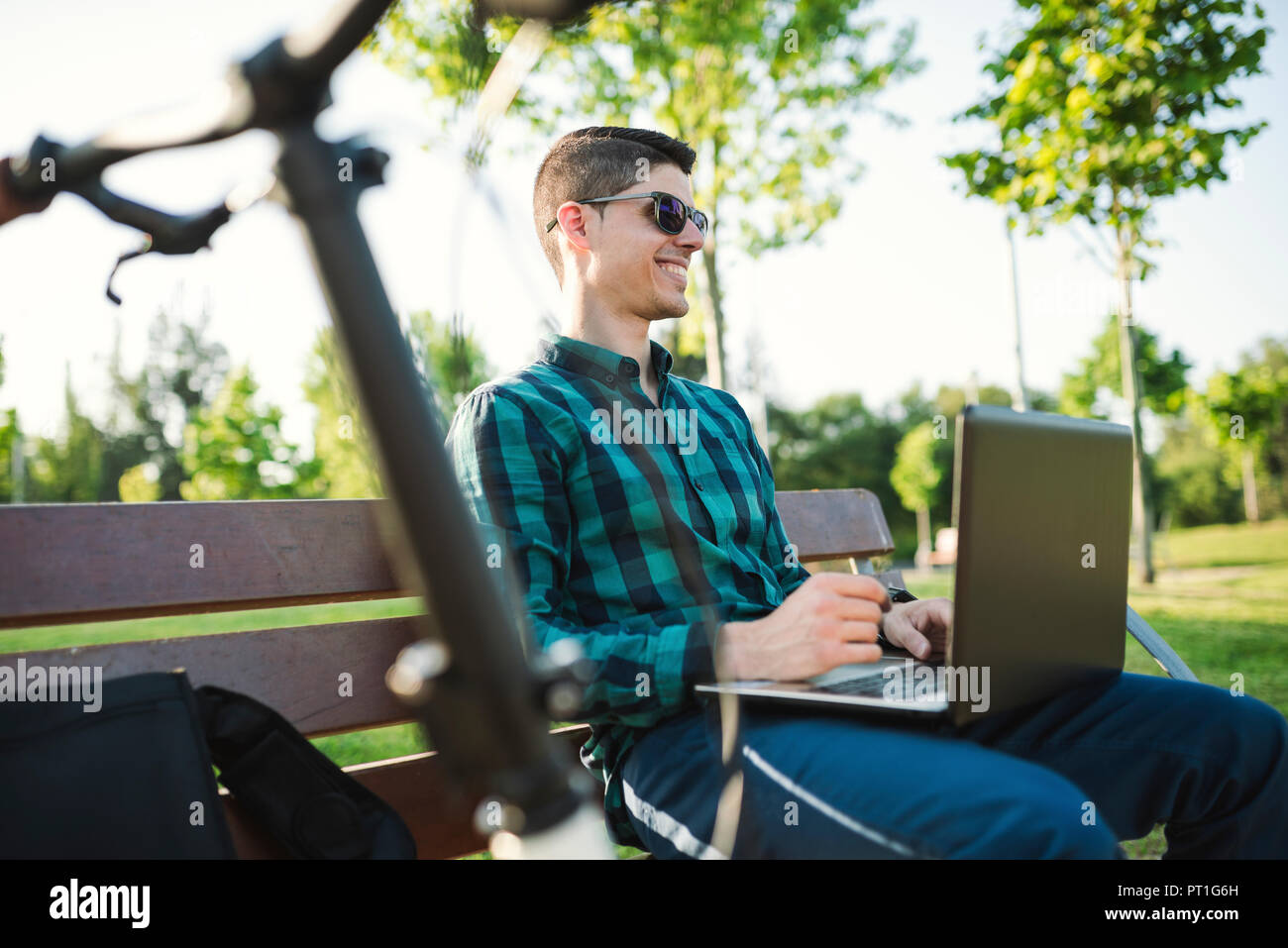 Young man with bicycle using laptop on park bench Stock Photo