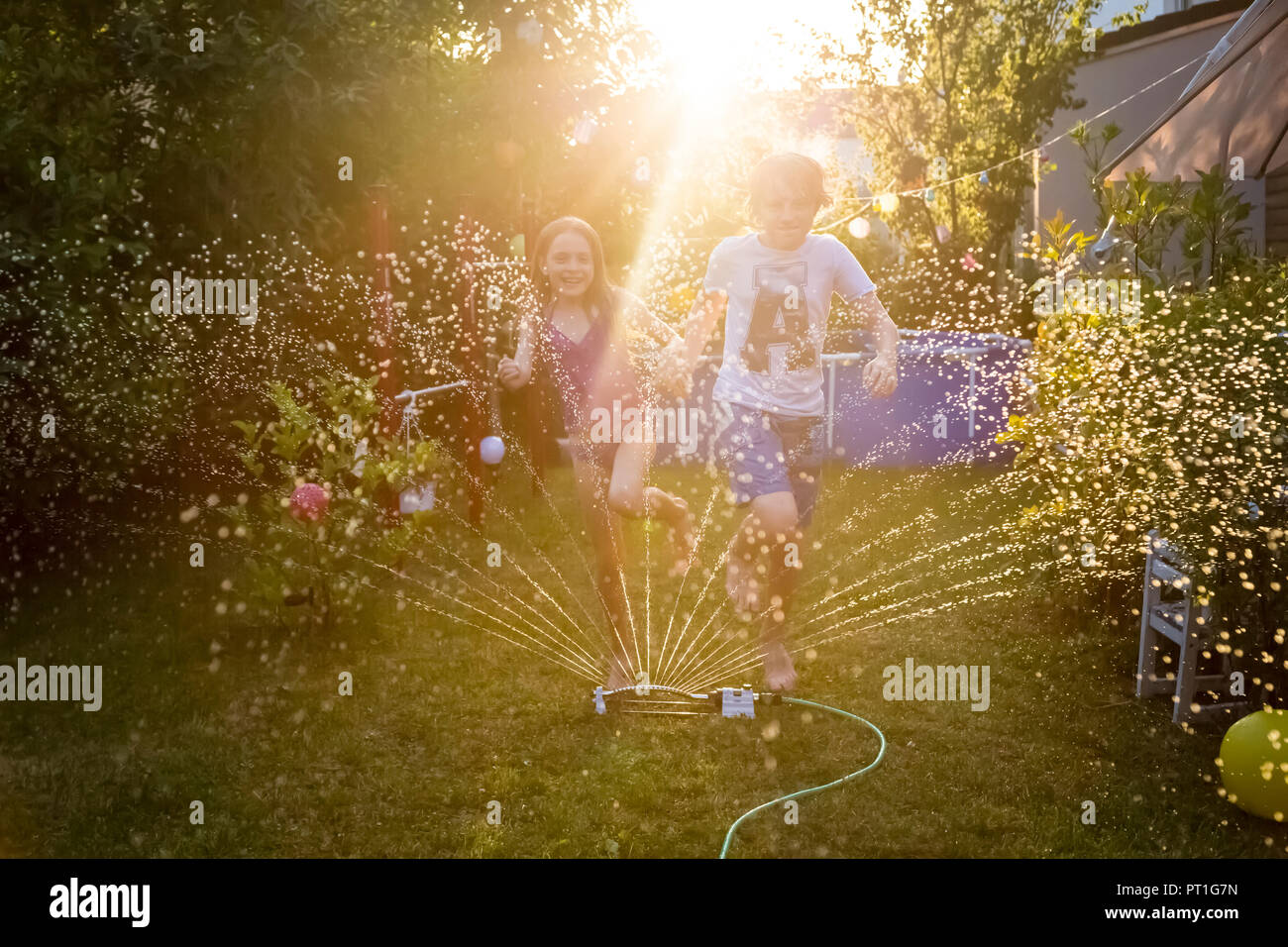 Brother and sister having fun with lawn sprinkler in the garden Stock ...