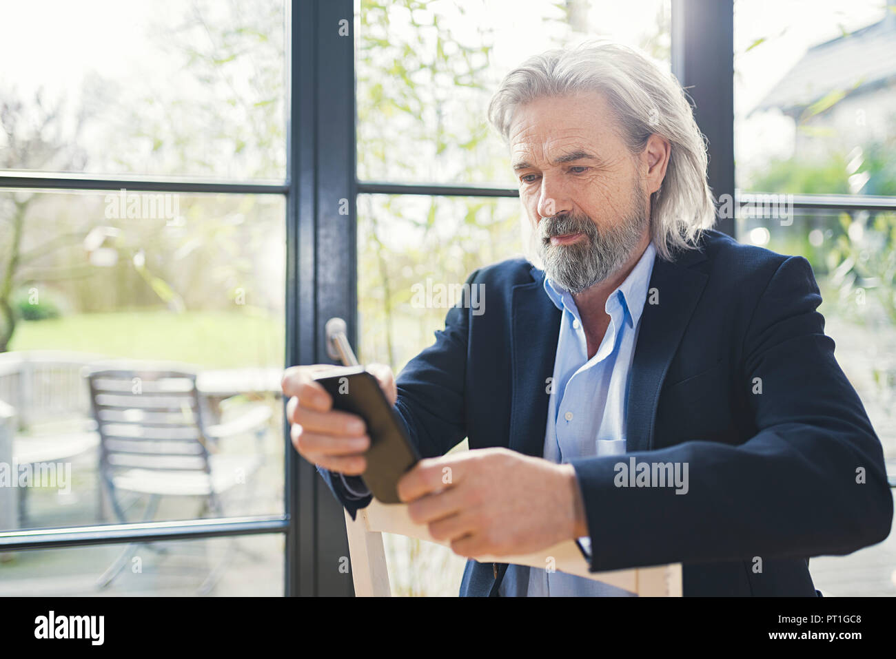 Senior businessman sitting on chair, using smartphone Stock Photo