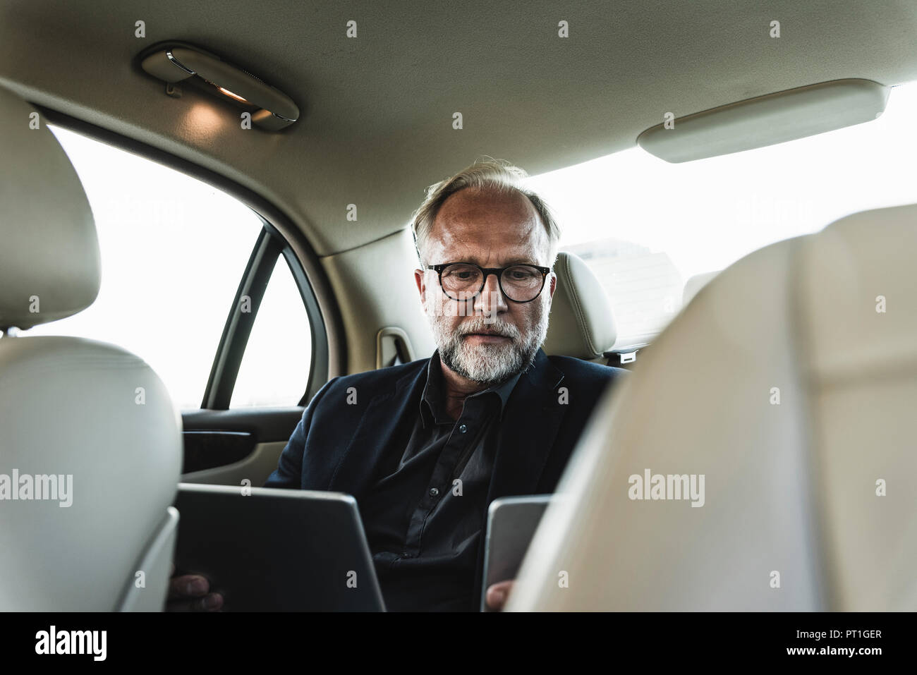 Mature businessman sitting on backseat in car, using digital tablet Stock Photo