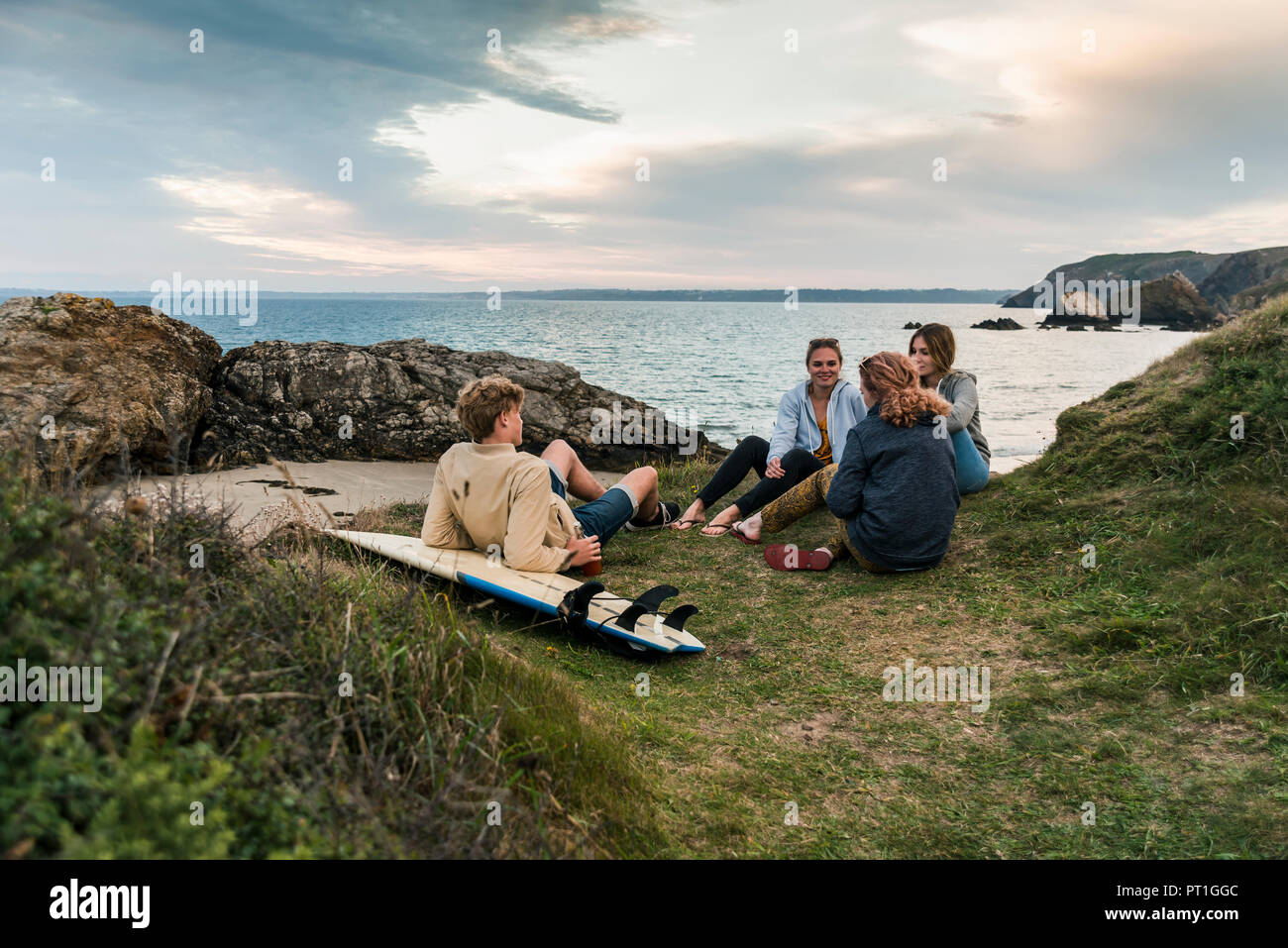 Happy friends with surfboard socializing at the coast at sunset Stock Photo