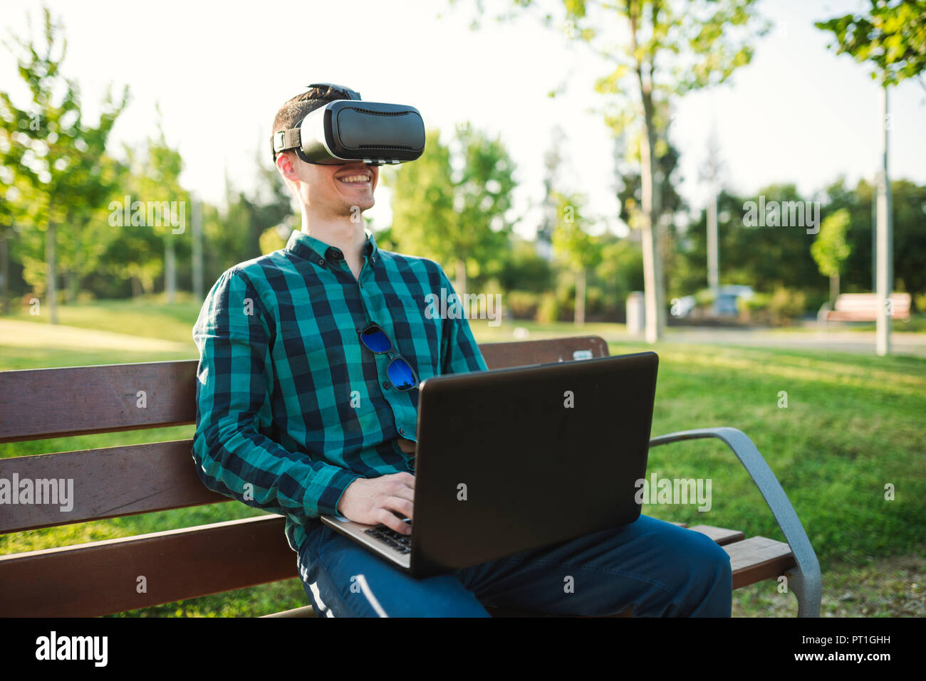 Young man working with VR glasses and laptop on park bench Stock Photo