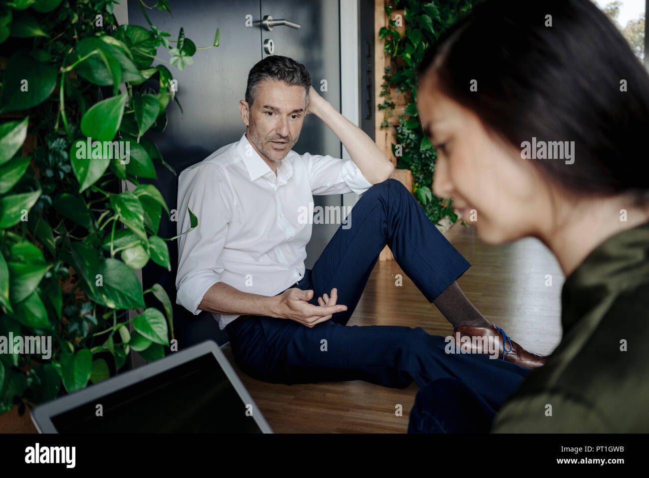 Businessman and businesswoman sitting on the floor in green office using tablet Stock Photo