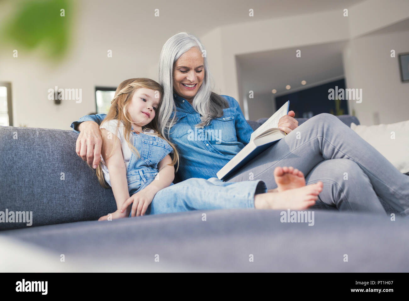 Grandmother and granddaughter sitting on couch, reading together Stock Photo